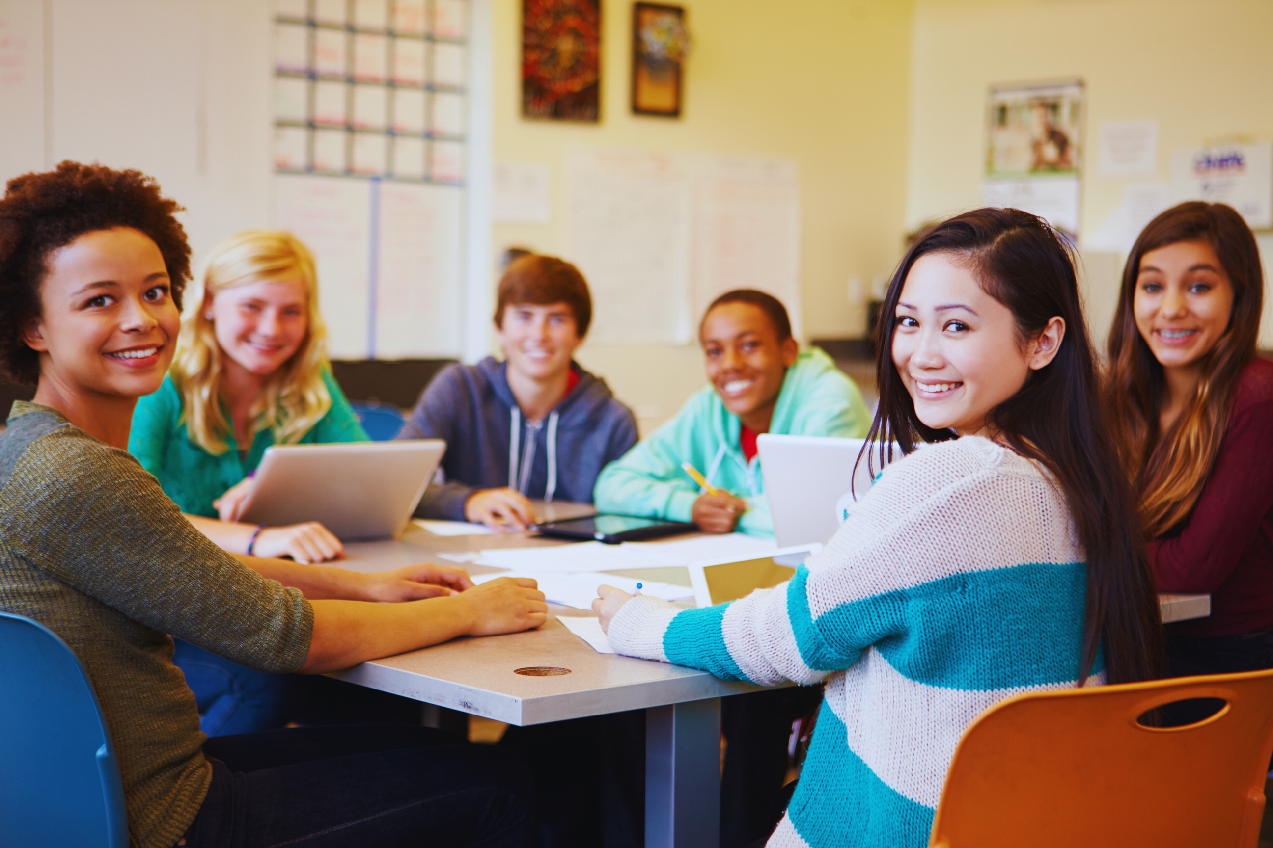 a group of high school students sitting at a table in a classroom smiling 